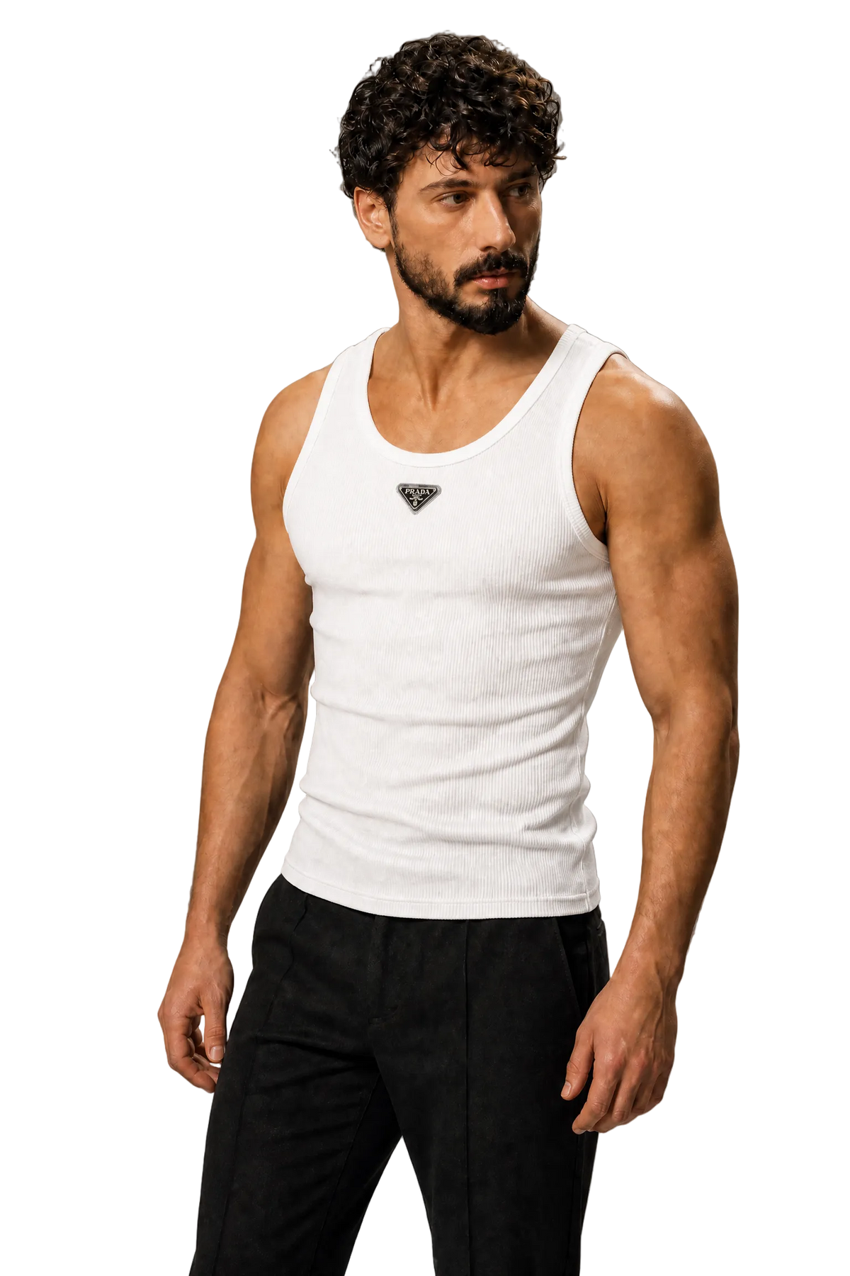 A muscular man with curly dark hair and a beard wearing a white ribbed tank top with a small black geometric logo on the chest, paired with black pants, standing against a textured gray studio background.