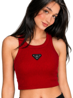 A woman wearing a red ribbed crop top with a small black triangular chest logo patch that reads 'alo', photographed against a plain light gray studio background.