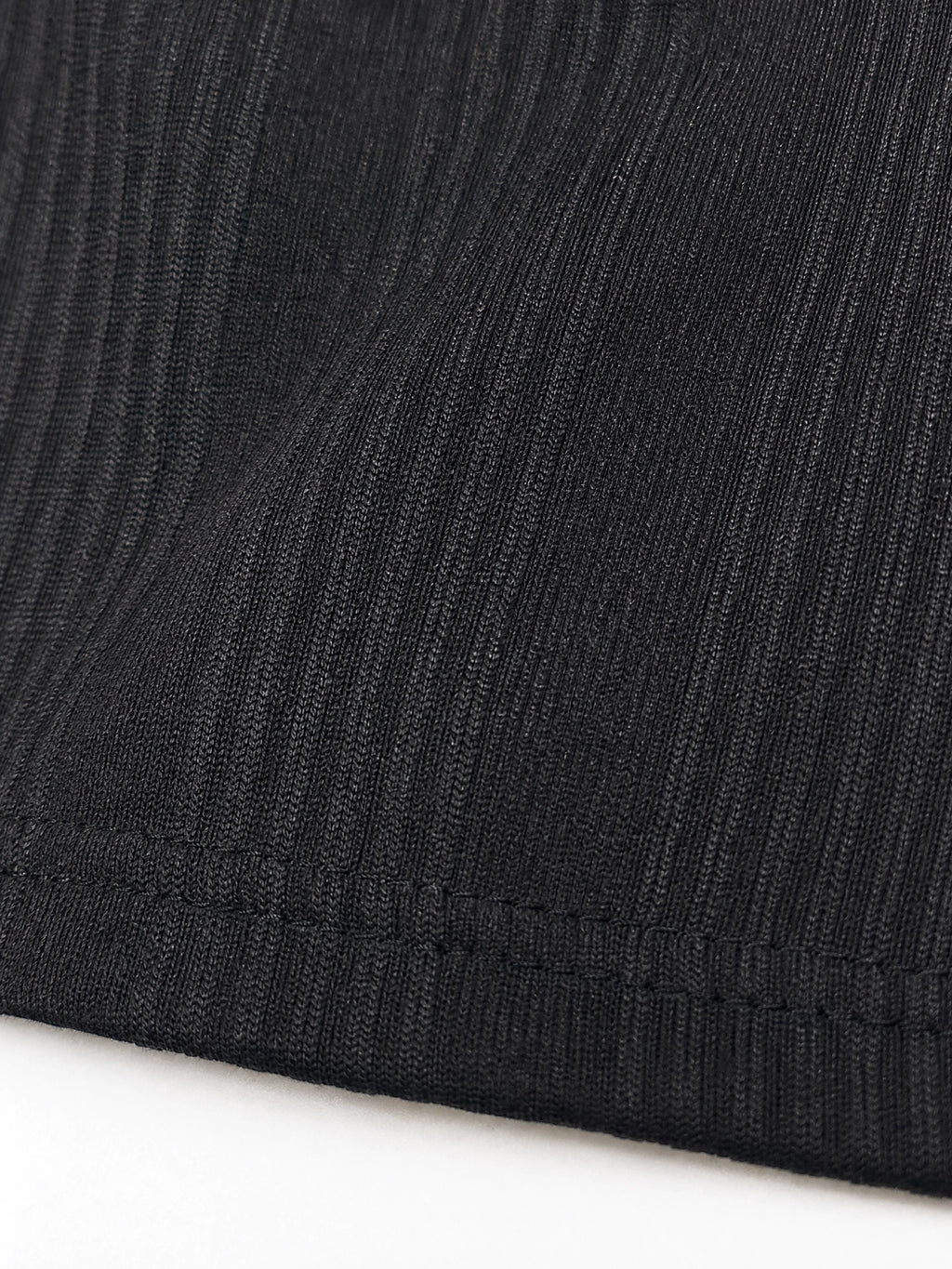 Close-up of a black ribbed knit fabric with a hemmed edge, showing the texture and stitch detail against a white background.