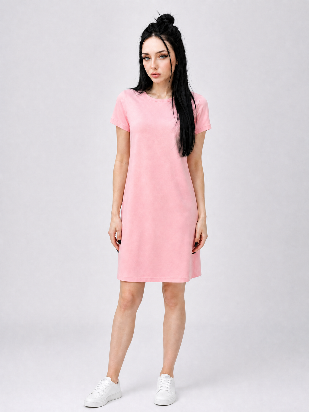 A woman modeling a short-sleeve pink dress with a crew neck, paired with white sneakers, against a light gray studio background.