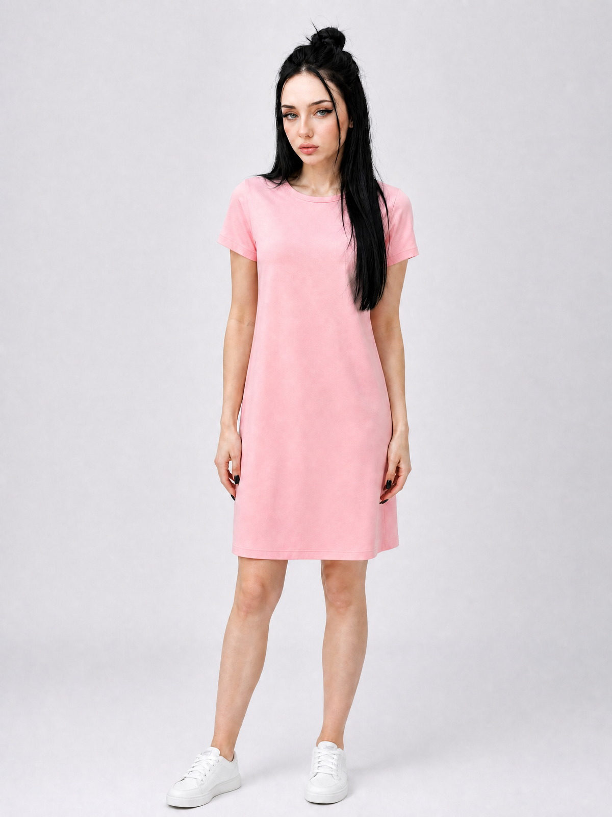 A woman modeling a short-sleeve pink dress with a crew neck, paired with white sneakers, against a light gray studio background.
